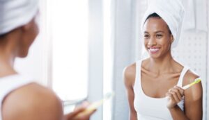 Smiling woman brushing her teeth in front of mirror